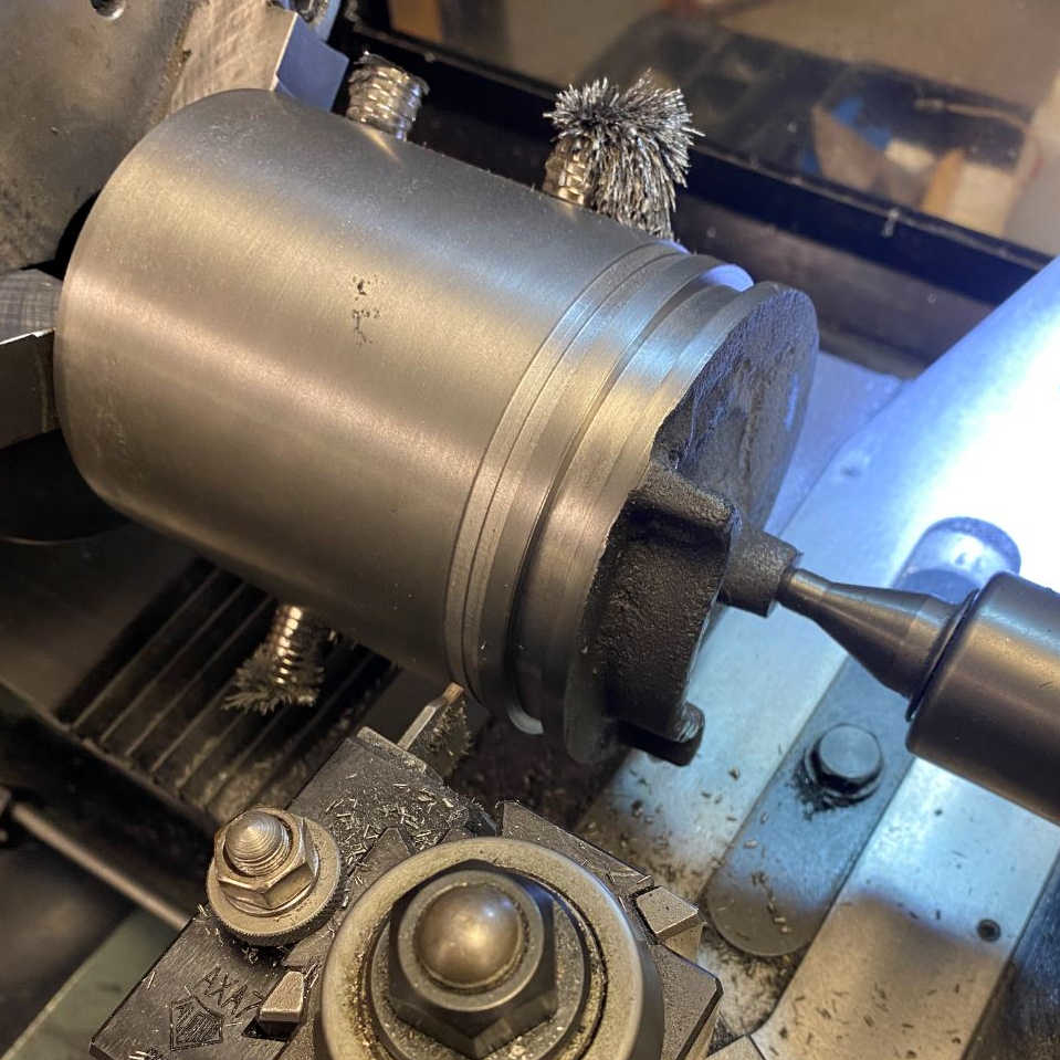 After turning the Piston OD to its finished dimension, the ring grooves are cut with a carbide parting tool. The magnets stuck on piston are an old machinist's trick for reducing chatter by adding some extra damping to the part.